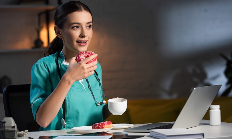 Attractive,Nurse,In,Uniform,Sitting,At,Table,And,Eating,Donut